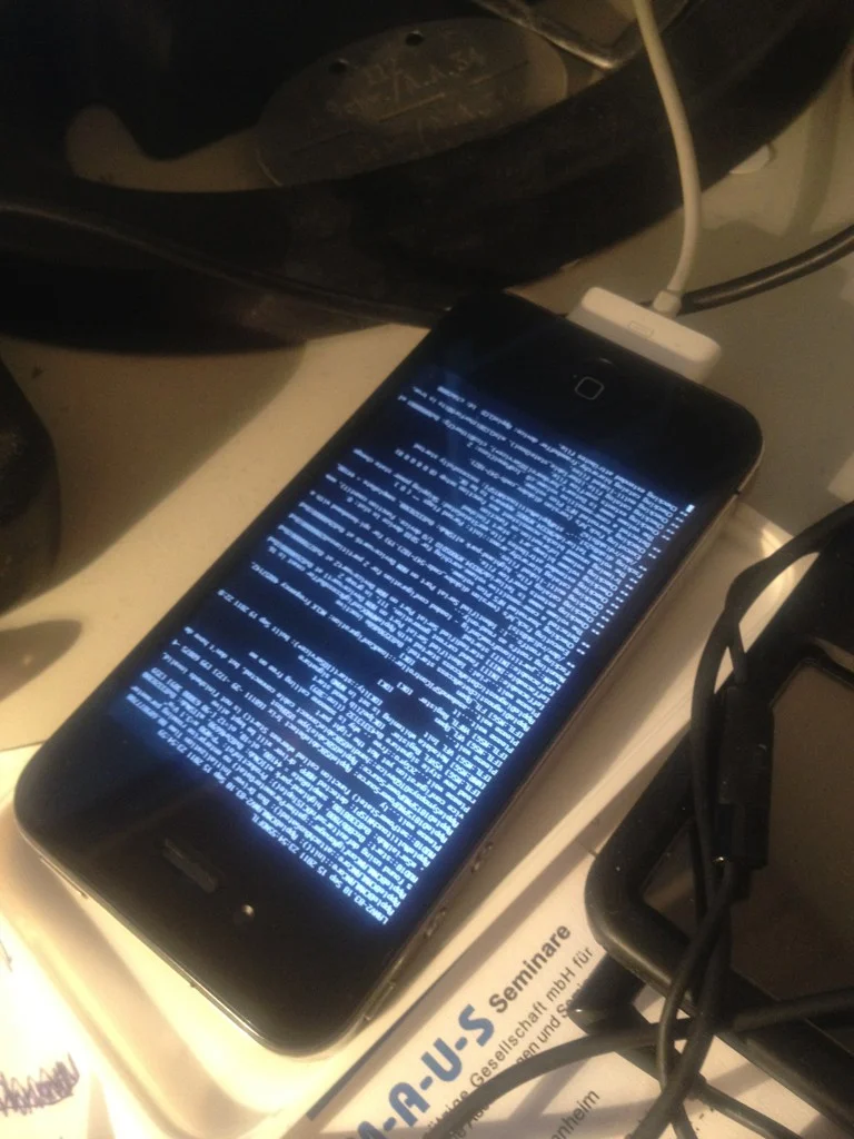 Ein schwarzes Smartphone mit blauem Code-Text auf dem Bildschirm liegt auf einer weißen Oberfläche neben einem Seminar-Zertifikat.