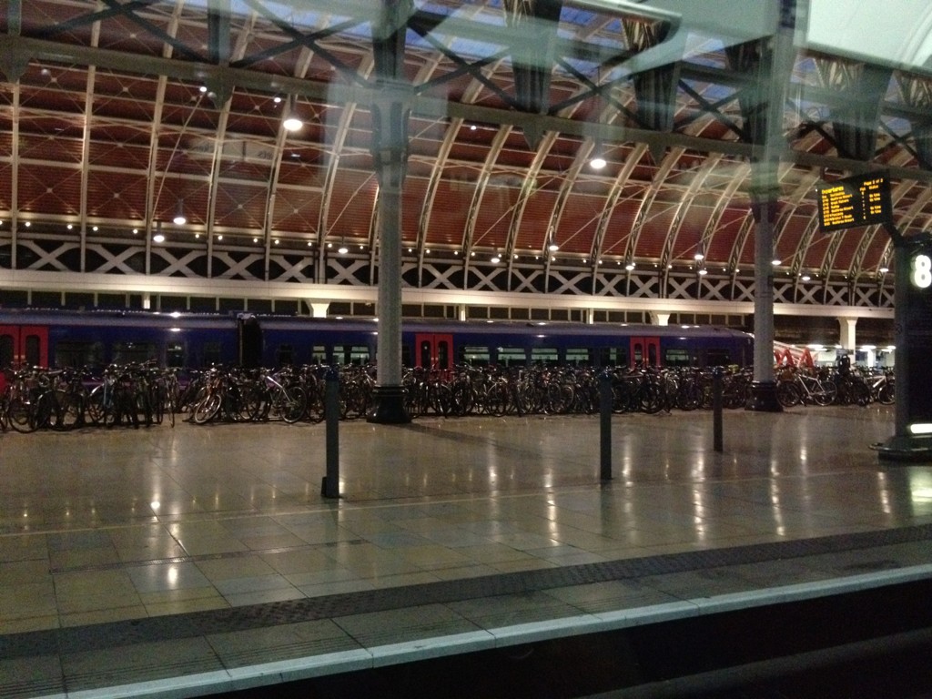 Großer überdachter Bahnhof mit hunderten abgestellten Fahrrädern entlang der Bahnsteige in der Abenddämmerung.