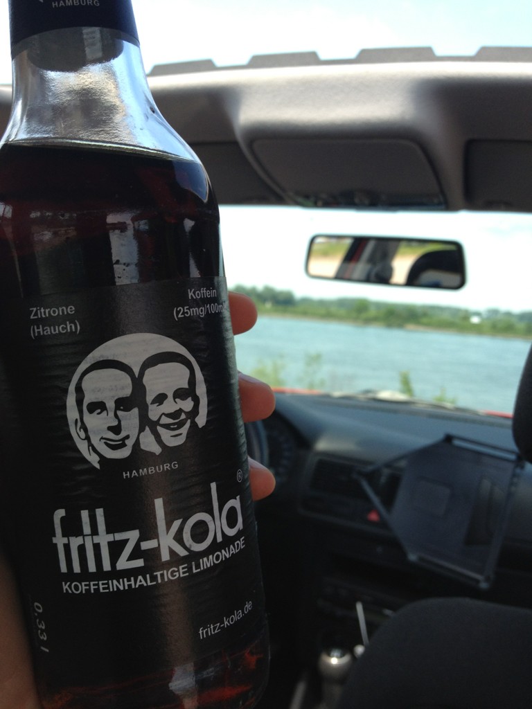 Eine Flasche fritz-kola Limonade wird in einem Auto vor einem Fluss gehalten.