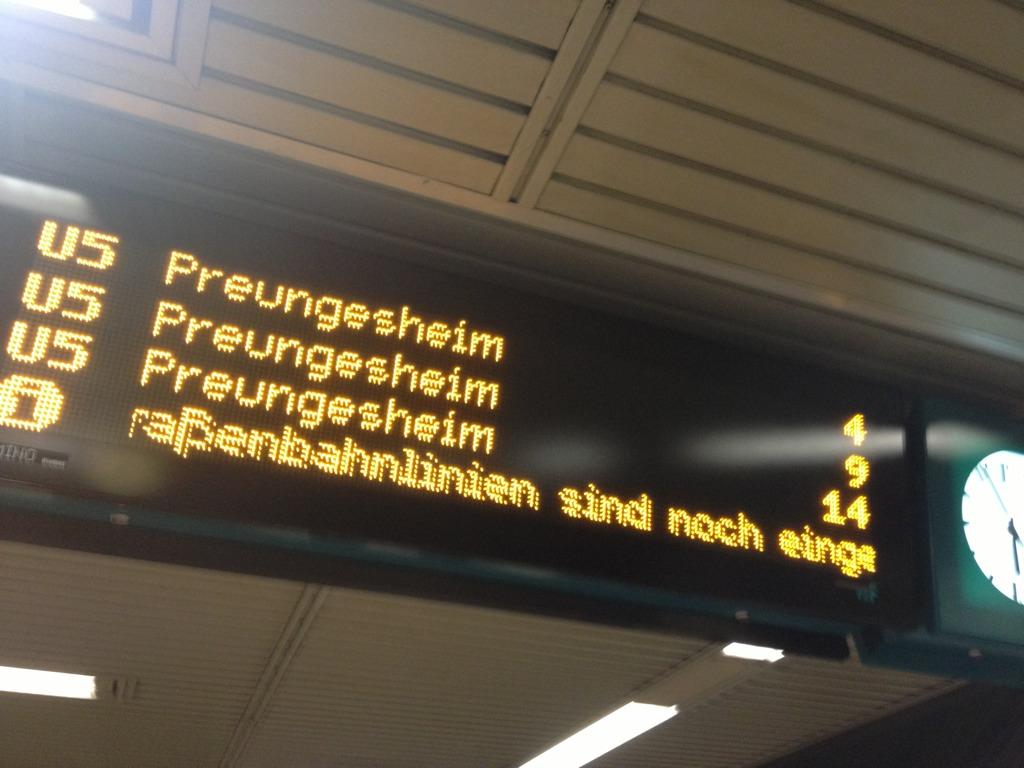 Anzeigetafel mit gelben Leuchtbuchstaben zeigt mehrere Züge nach Preungesheim und eine Durchsage über Verspätungen an.