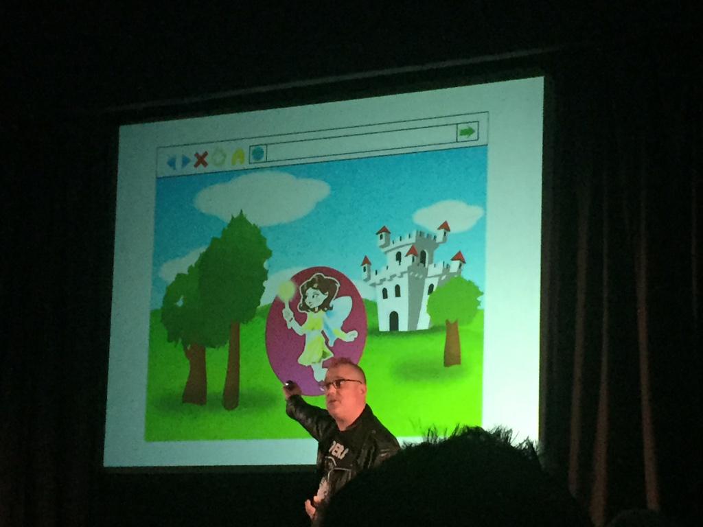 Ein Mann mit Brille zeigt auf eine projizierte Illustration mit einer Prinzessin, Bäumen, einem Schloss und einer grünen Landschaft.