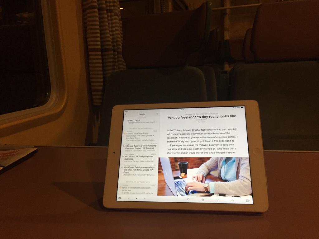 Ein Tablet mit orangefarbenem Rahmen zeigt einen Artikel mit dem Titel "What a freelancer's day really looks like" auf einem Tisch in einem dunklen Innenraum.