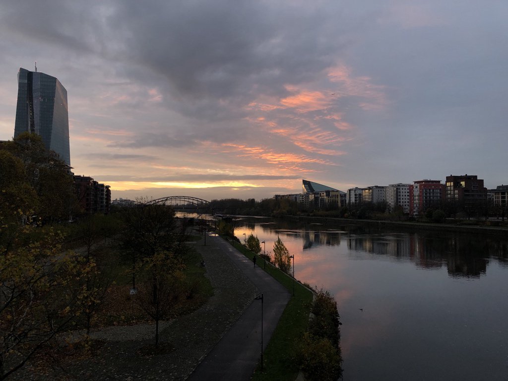 Sonnenuntergang über einem Fluss in einer Stadt mit modernen Hochhäusern und einer Brücke im Hintergrund.