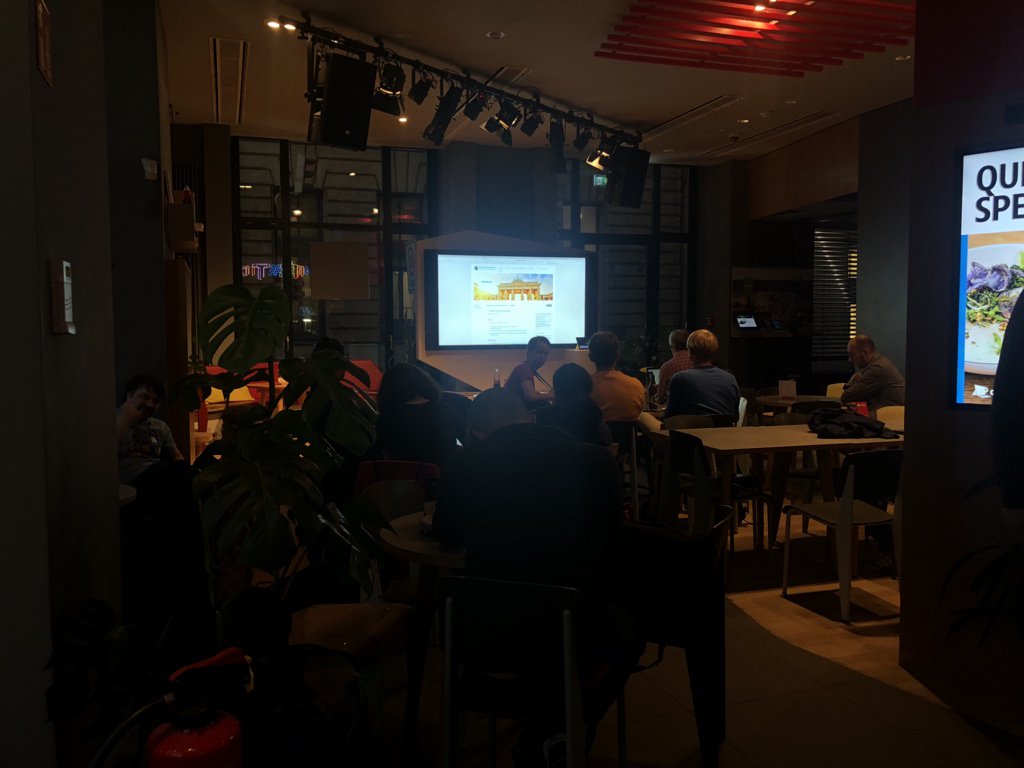 Eine Gruppe von Menschen sitzt in einem modernen Veranstaltungsraum und beobachtet eine Präsentation auf einem Bildschirm an der Wand.