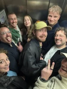 Ein Aufzug voller Menschen, die alle lächeln und albern in die Kamera schauen.