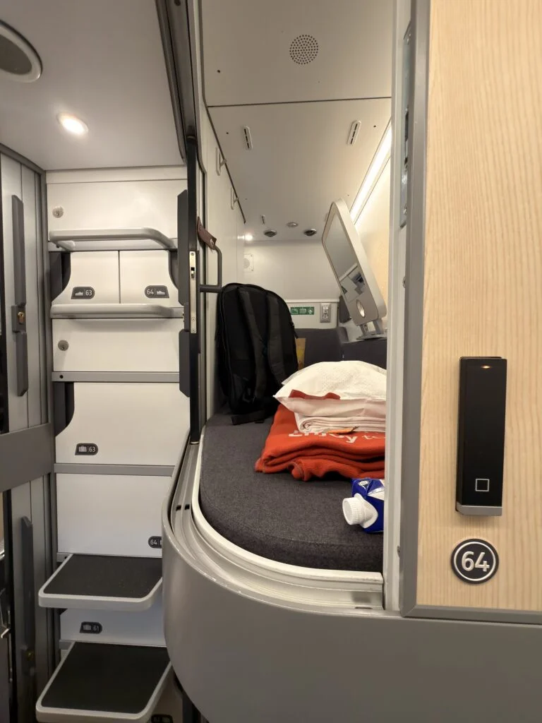 Eine Schlafkabine im Schlafwagen des Zugs. Ein Rucksack, Decke und Bettlaken liegen in der Kabine.