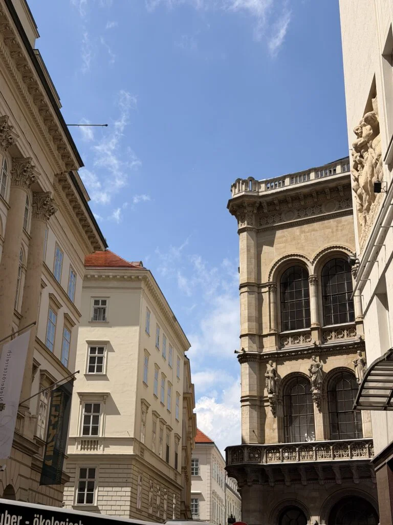 Enge Gasse in einer europäischen Stadt mit klassischen Gebäuden und einem ornamental verzierten Kirchturm unter blauem Himmel.