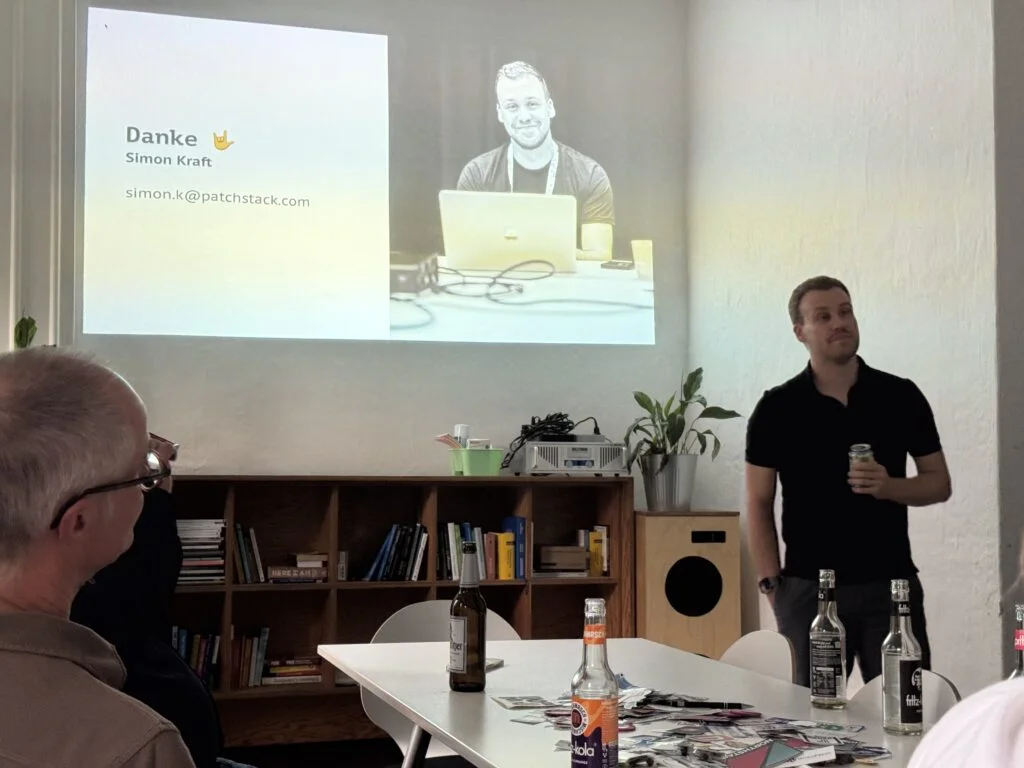 Simon in schwarzem Poloshirt spricht vor einer Gruppe und zeigt eine Präsentationsfolie mit dem Namen Simon Kraft und seiner E-Mail-Adresse.