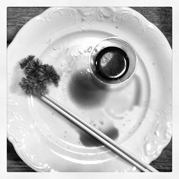 An empty plate on a table, chopsticks and some soy sauce on top of it