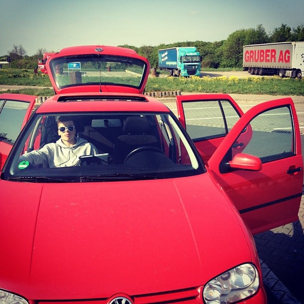 A red car, in a parking lot. Trucks in the background.