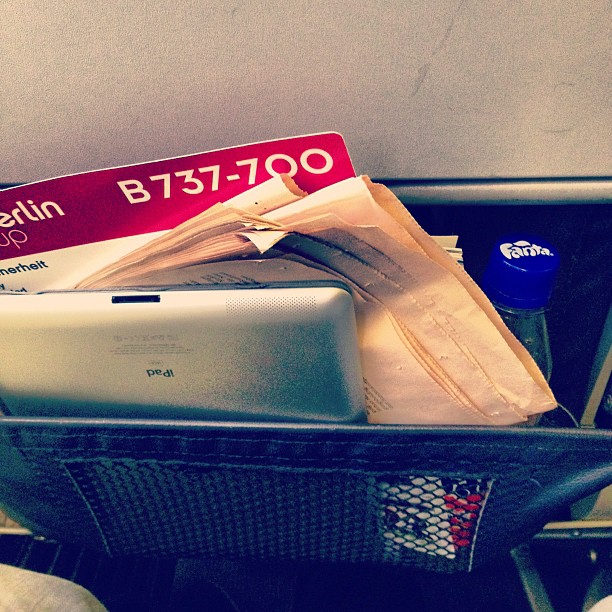 An iPad in the pouch of and airplane seat next to the emergency pamphlet readying "Air Berlin, B737-700"