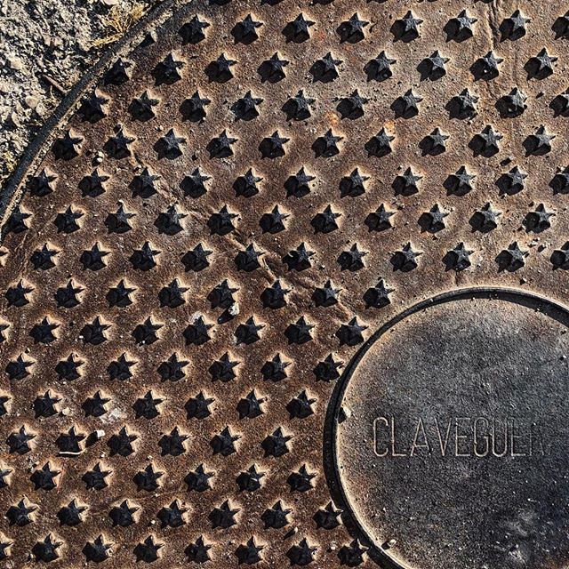 Top view of a manhole cover. In frame is only a quarter, covered in a star pattern.