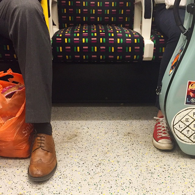 Two people sitting one seat apart in the subway. only one leg per person in frame