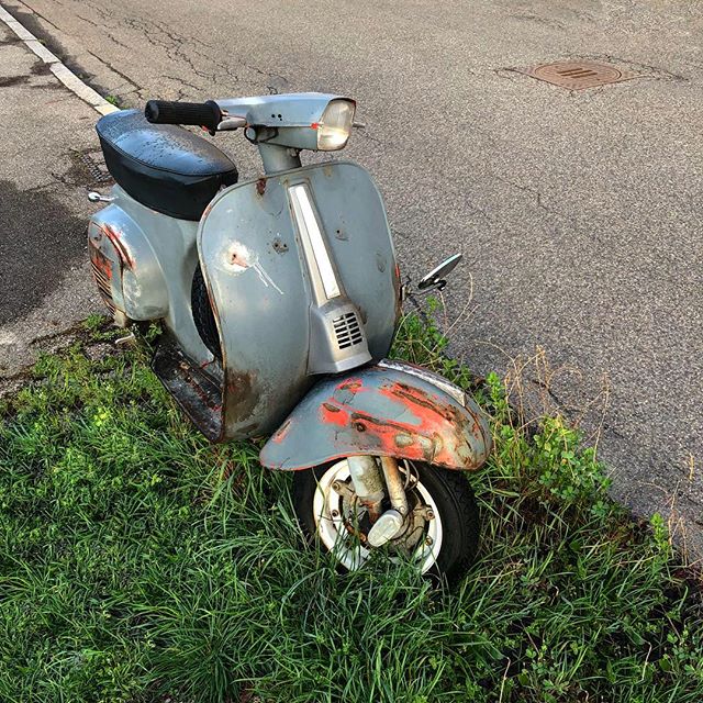 Rusty old Vespa scooter on a patch of grass by the roadside