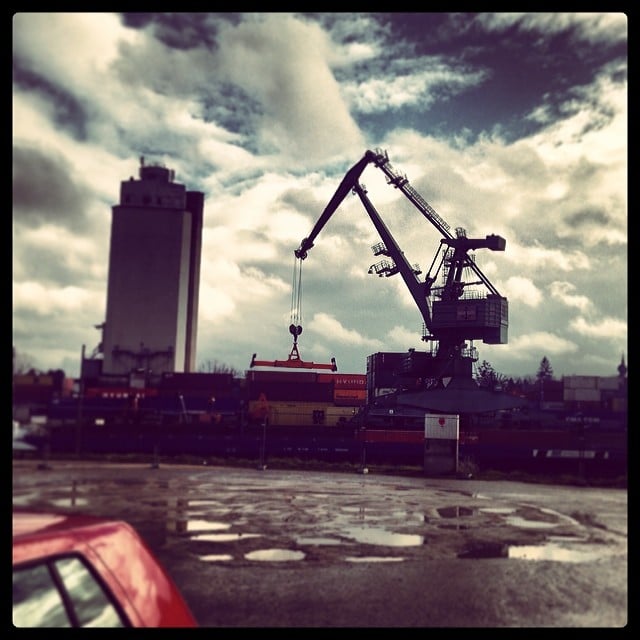 A red car on the left, some containers in the back, a big cargo crane towering over them