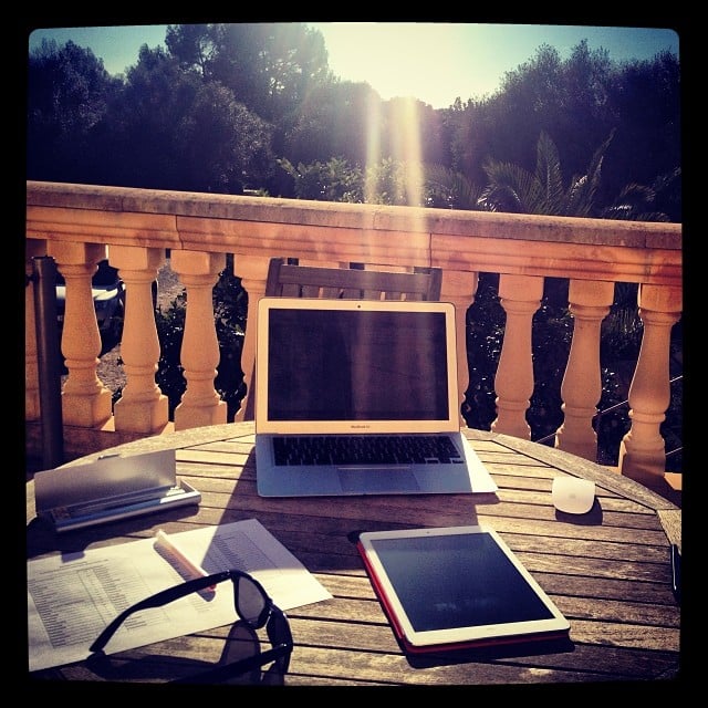 A tabel on a sun deck with a computer, a tablet, some paper and pens