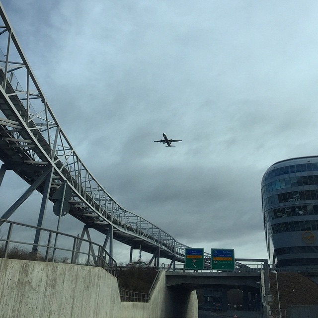 A high railway on the left, street on the bottom with an airplane flying above (landing)