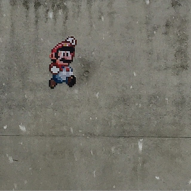 a pixelated version of Nintendos Mario on a grey concrete wall, depicted jumping