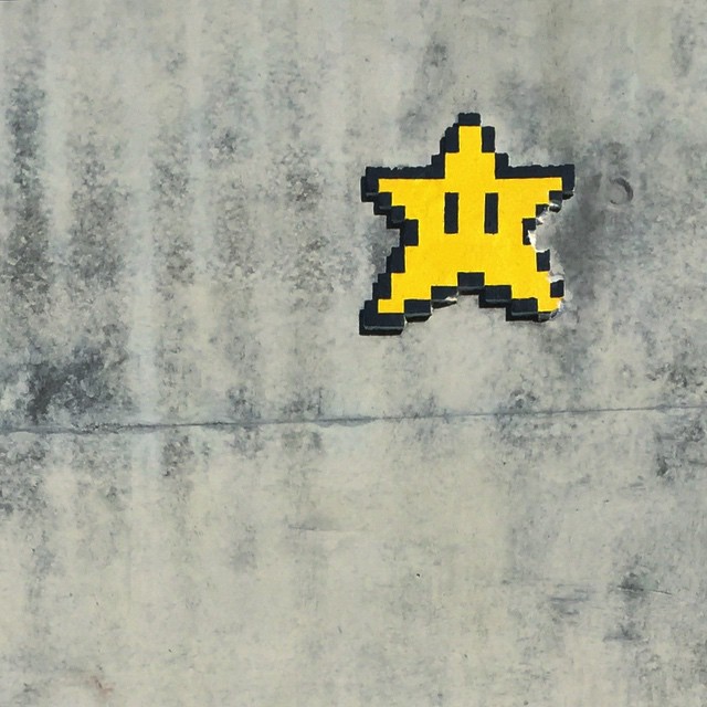 a pixelated version of a star from Nintendo's Mario on a grey concrete wall