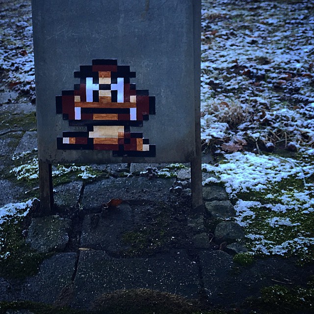 a pixelated version of a Goomba, a small brown mushroom with eyes and legs from Nintendo's Mario, on a trash can