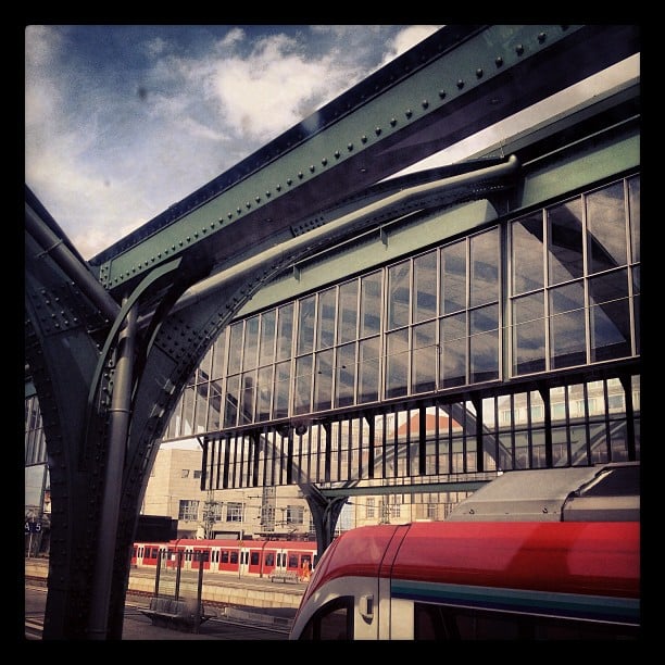 Steel roofing of a train station with bright red trains underneath