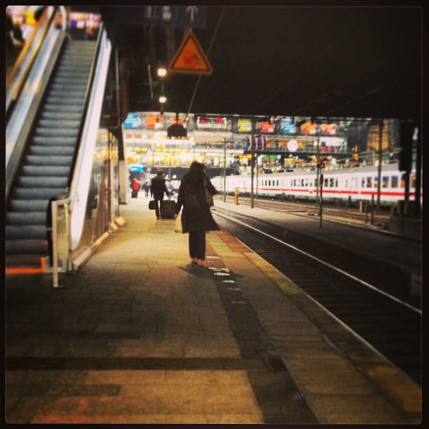 Train platform with a person walking away from the camera, a train in the distance on another track