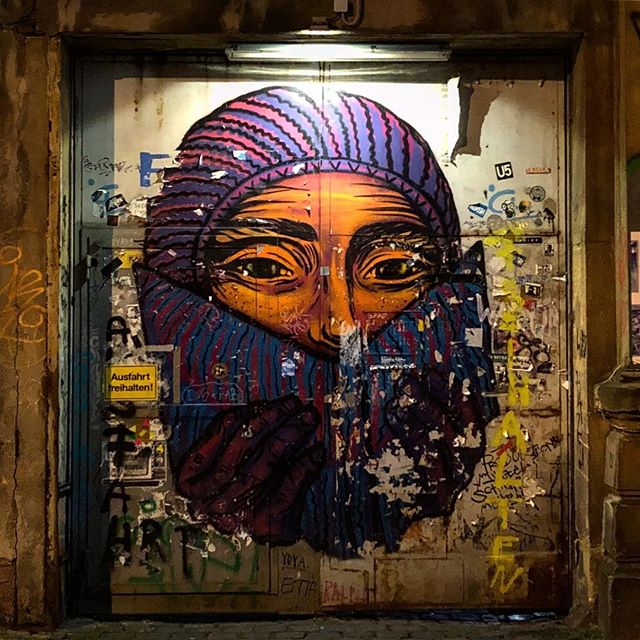 Streetart of a hooded and masked face, wrapped in vibrant pink cloth on a big metal door