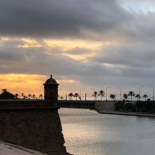 Silhouette of a small tower, sunrise behind the clouds in the background. A pond underneath.