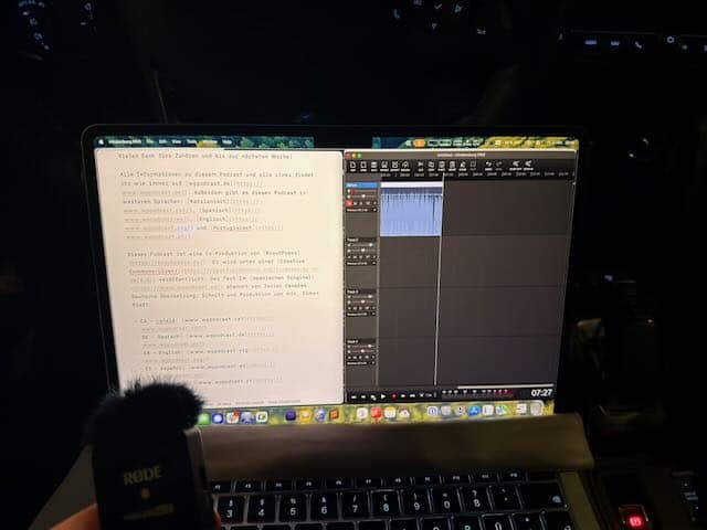 A brightly lit MacBook in an otherwise dark environment. In the background there are some illuminated buttons of a car's dashboard. In front of the MacBook, a small mic can be seen.