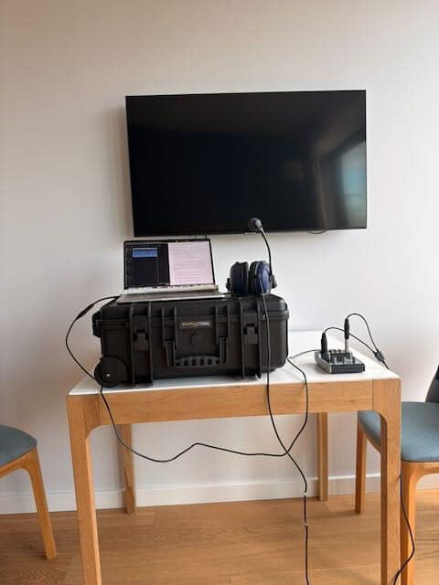 A open MacBook on a black tactical case with a headset and an an external audio interface all resting on a small square table.