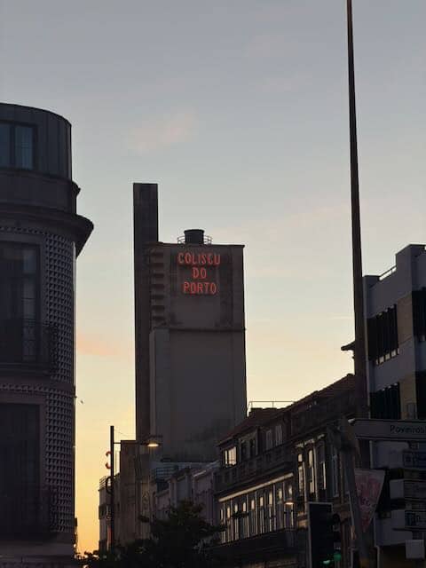 A tall building with a Portuguese neon sign against the backdrop of a late sunset