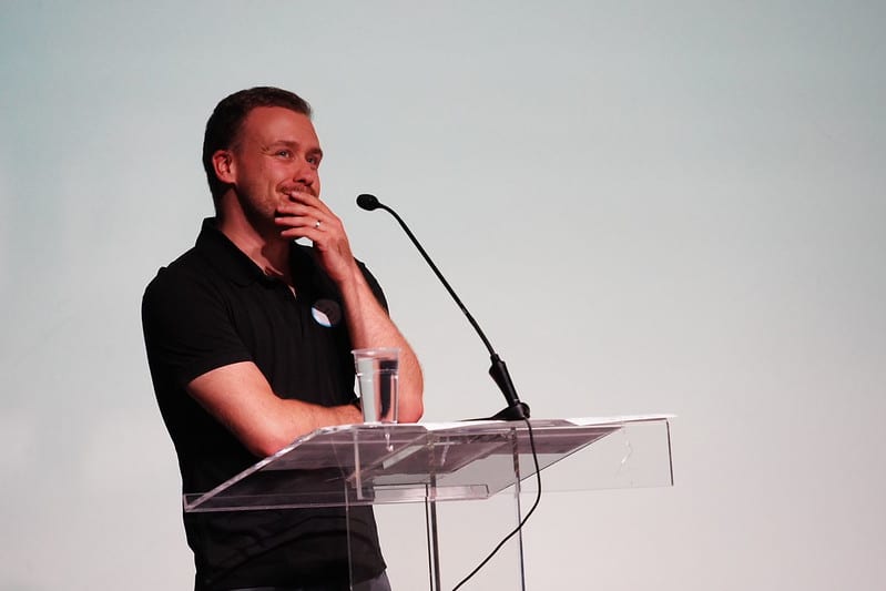 Simon in front of a white projector screen. Smiling.
