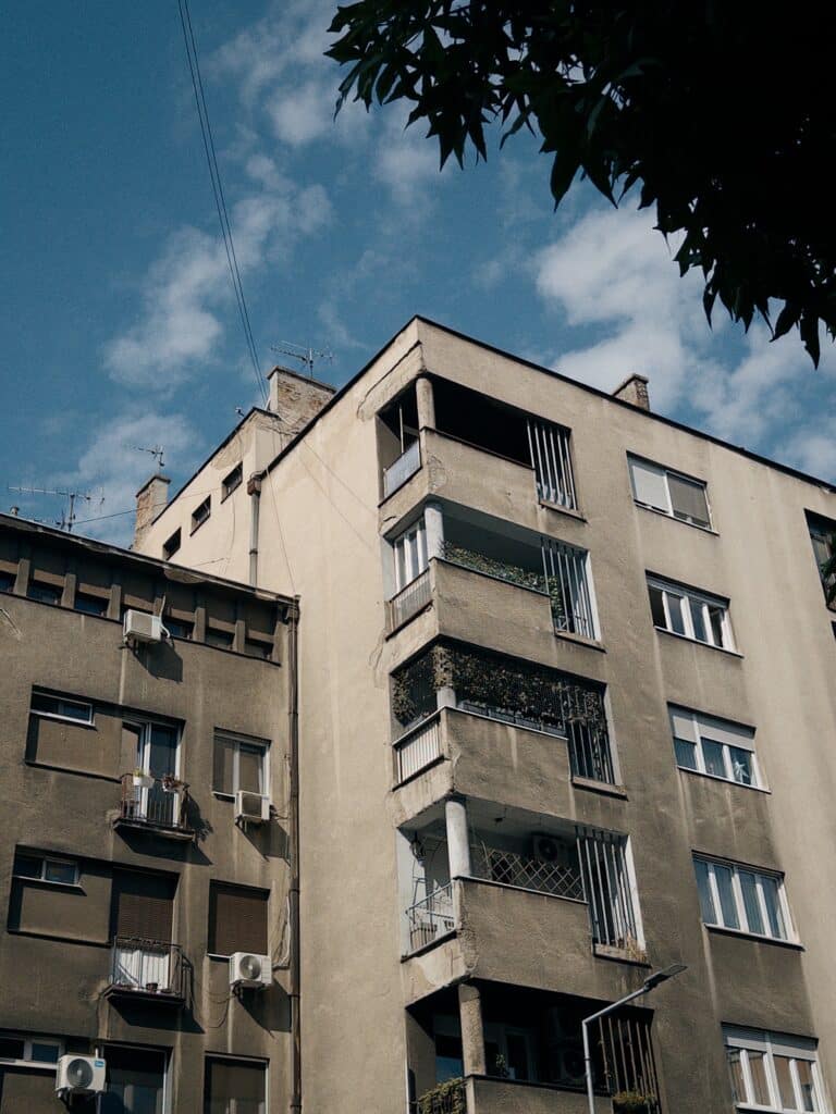 A grey concrete building with balconies and AC units. Blue sky with some light clouds as a backdrop.