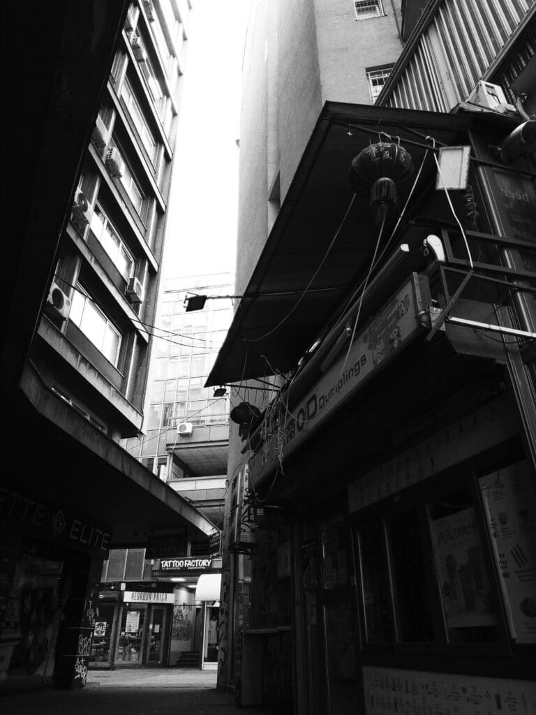 Black and white photo of a narrow way between two high buildings. An asian restaurant on the the right makes the whole scenery feel like its set in Asia.