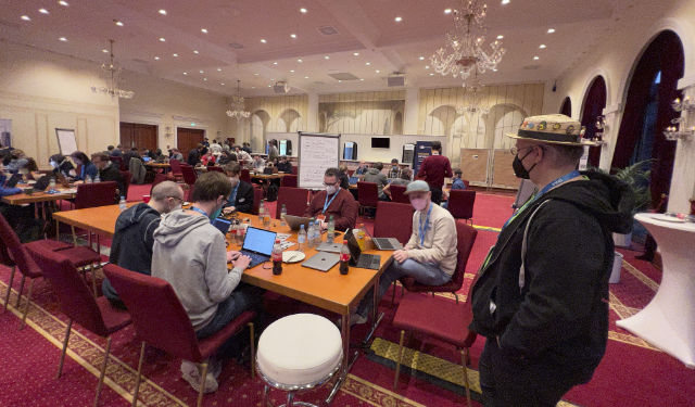 Das Antispam-Bee-Team sitzt gemeinsam an einem Tisch im Saal des Hackathons und arbeitet.